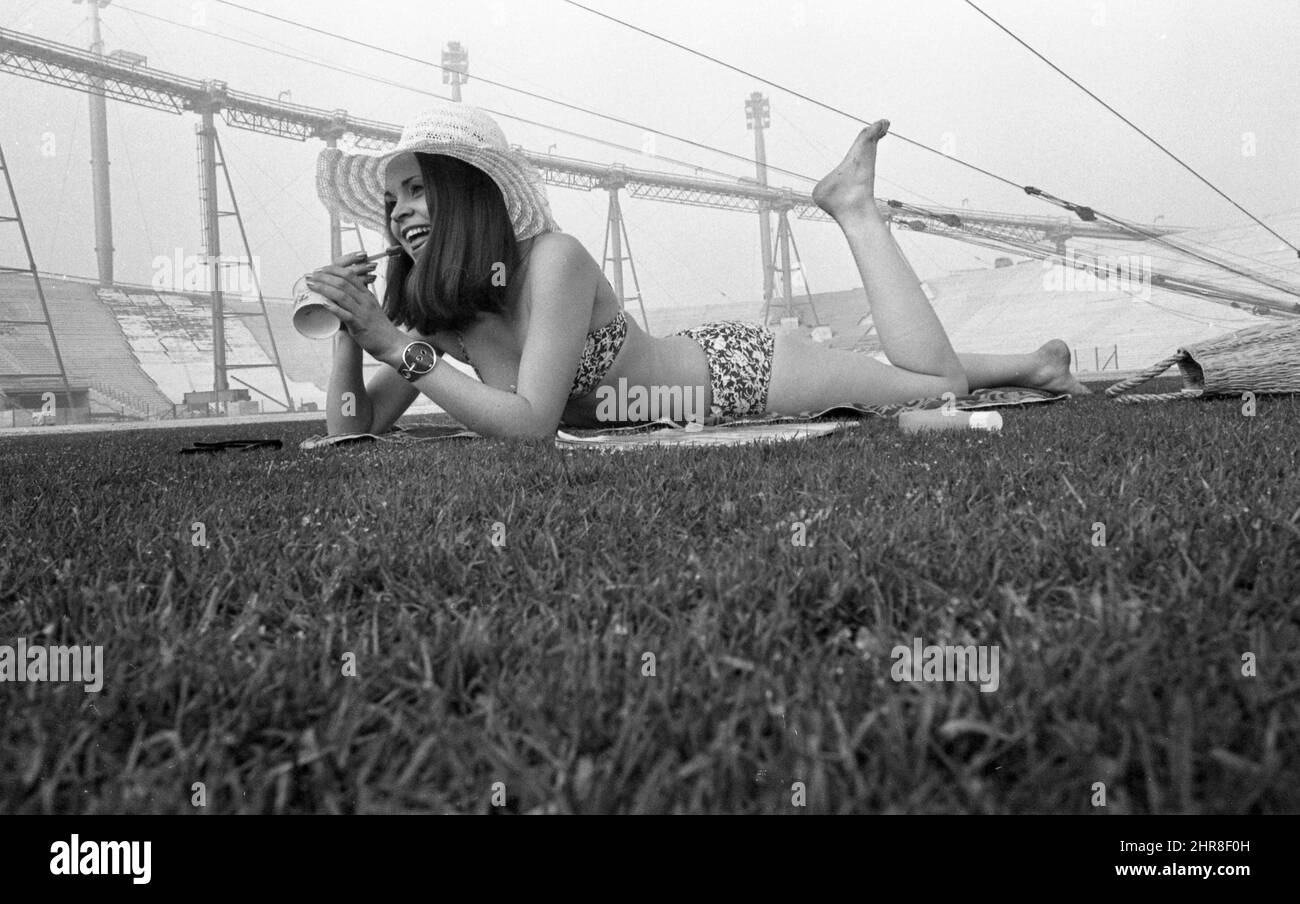 A young woman in a bikini is lying on the pitch of the Munich Olympic Stadium, snow can be seen in the background. The Munich Olympic Stadium was the first stadium in Germany with pitch heating, overview, panorama, architecture, black and white, black and white, black and white, monochrome, SW monochrome, black and white photo, Â Stock Photo