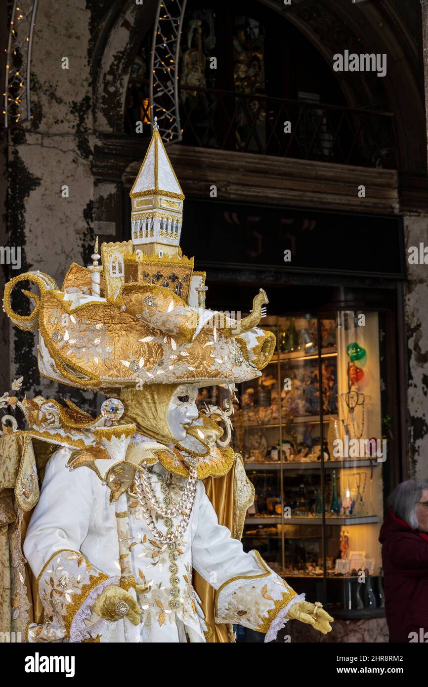 Venice, Italy. 25th Feb, 2022. Colourful costumes at the Carnival in Venice 2022. Man in costume wearing a large hat with Venetian landmarks in St. Mark's Square. Credit: Vibrant Pictures/Alamy Live News Stock Photo