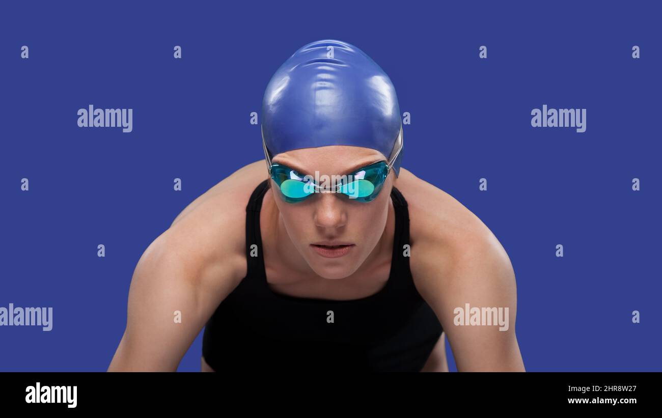 Swimmer woman on the start ready to jump to the pool. Studio portrait against solid blue background Stock Photo