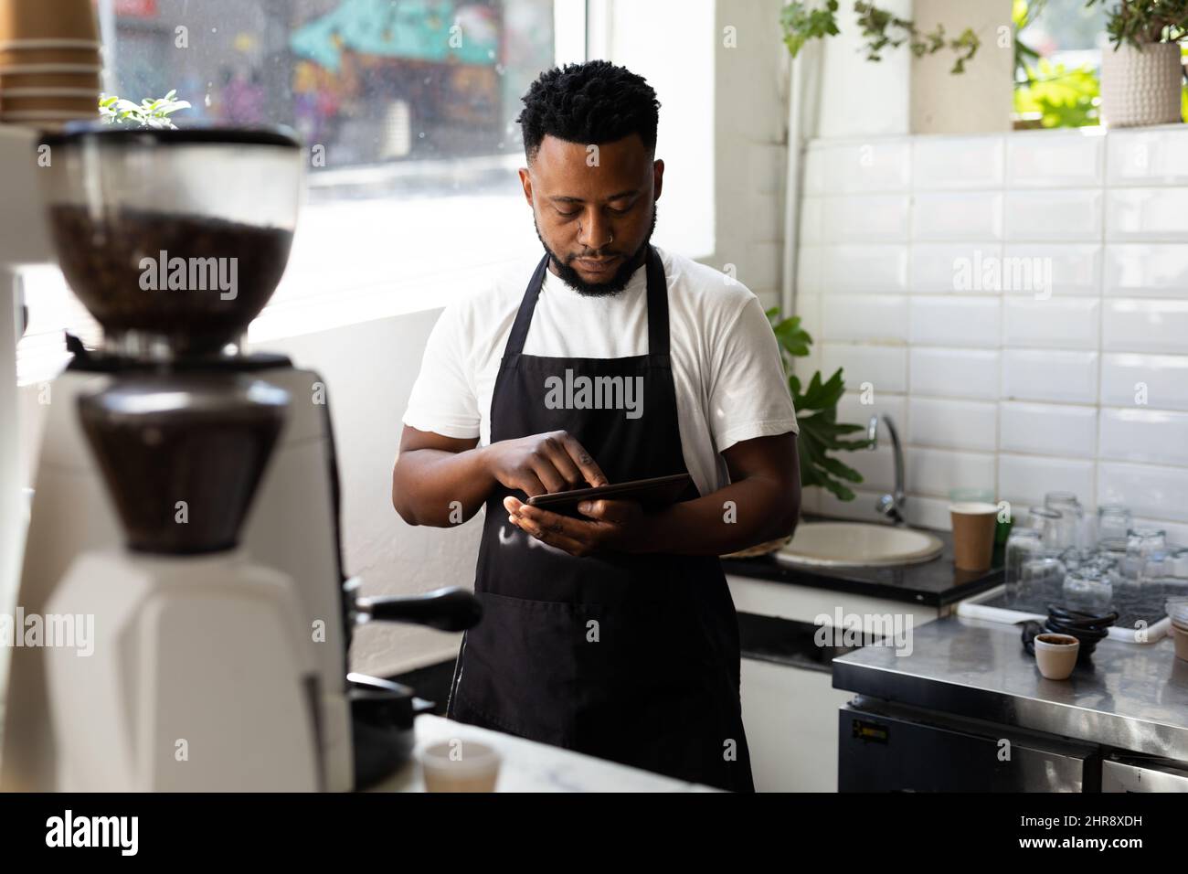 Young male african american barista using tablet pc while working in coffee shop Stock Photo