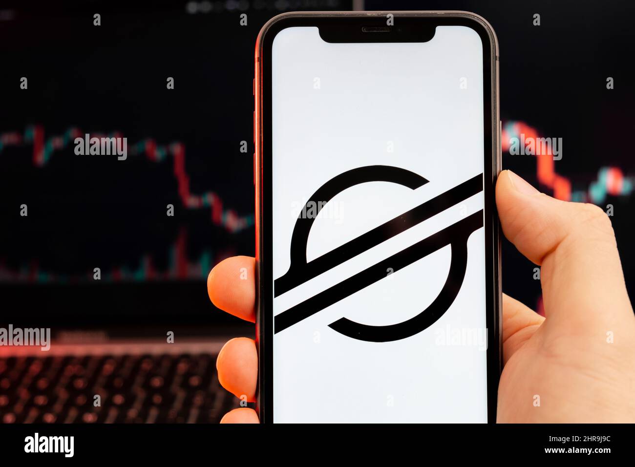 Stellar XLM cryptocurrency logo on the screen of smartphone in mans hand with downtrend on the chart on a red light background, February 2022, San Francisco, USA. Stock Photo