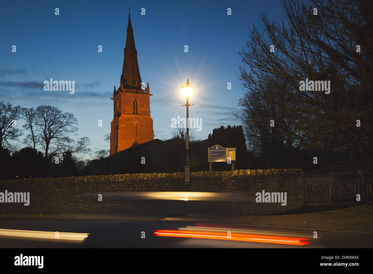 St Peter's Church, Sharnbrook, Bedfordshire, UK - Light trails from car speeding past parish church lit up at night Stock Photo