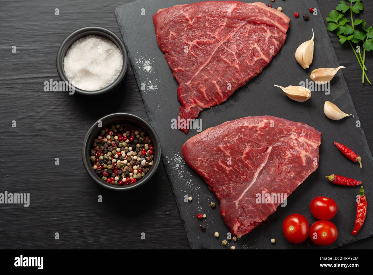 Raw meat steaks with cherry tomatoes, hot pepper, garlic, oil and herbs