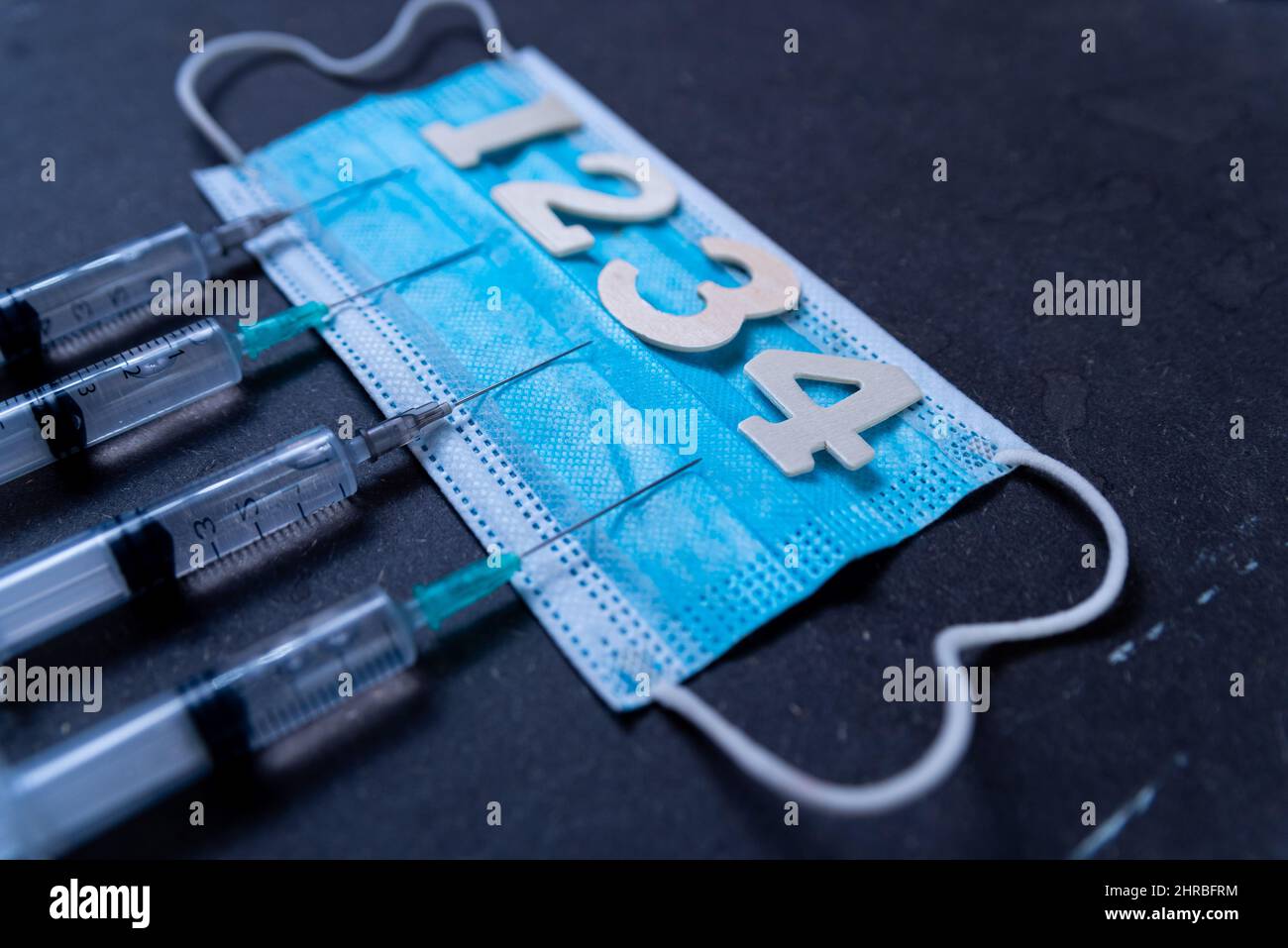 Fourth covid vaccine shot and jab concept with face mask. Four syringes are seen on table as a concept for the 4th covid-19 vaccine dose, also called Stock Photo