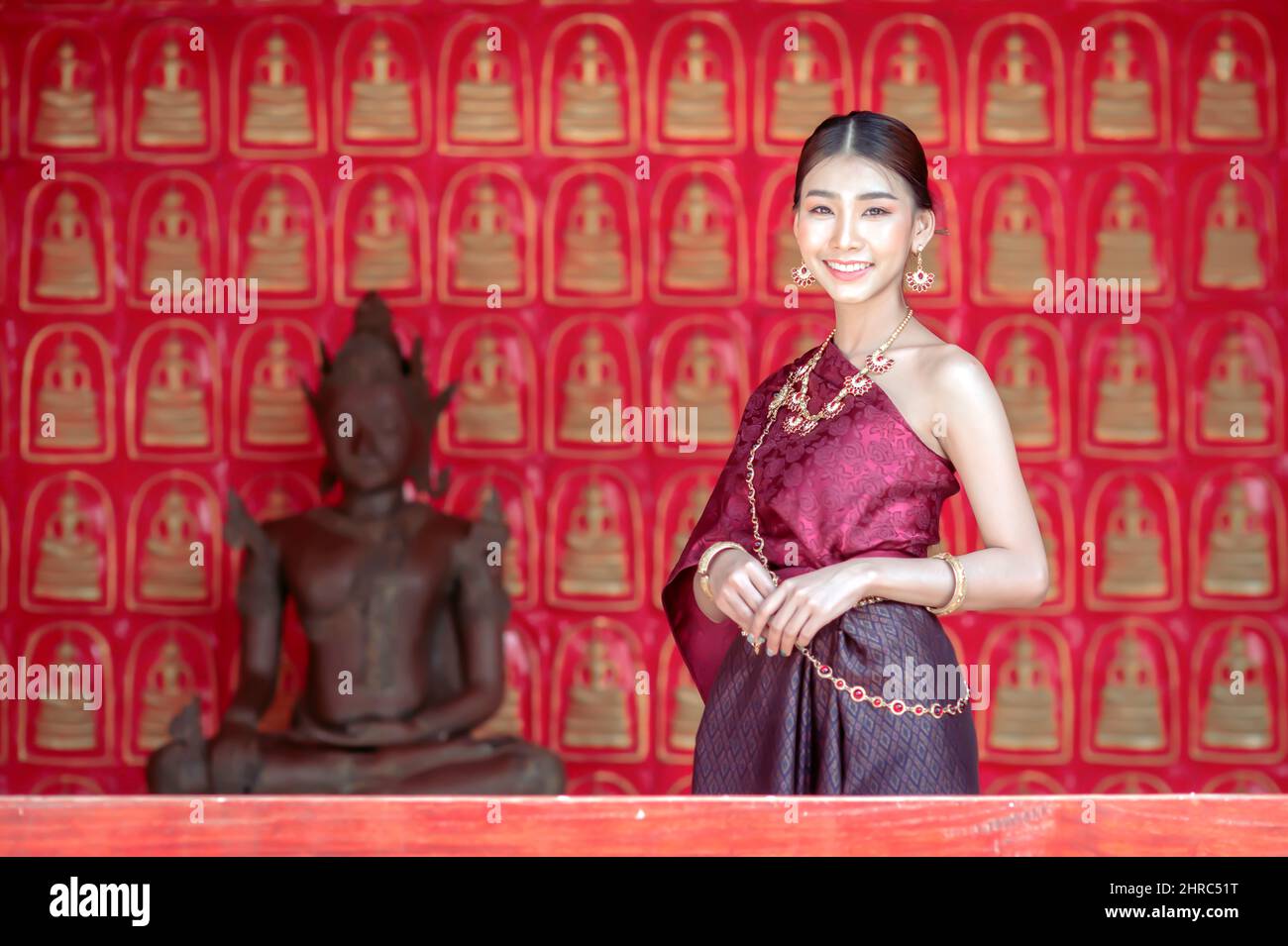 Portrait of a smiling woman in traditional clothing standing by a Buddha statue, Chiang Mai, Thailand Stock Photo