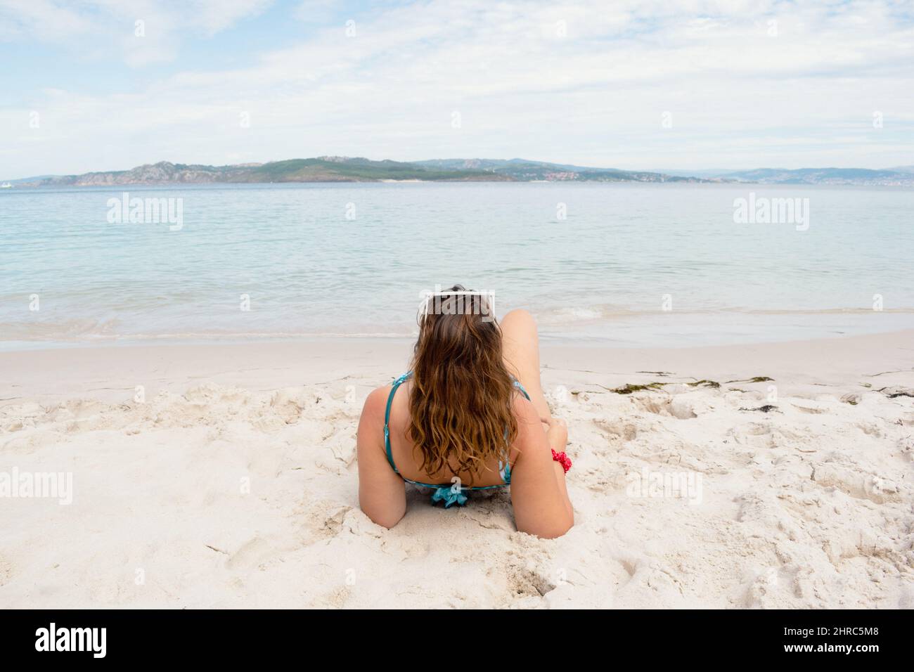 Rear view of a woman in a bikini lying on beach by water's edge, Spain ...