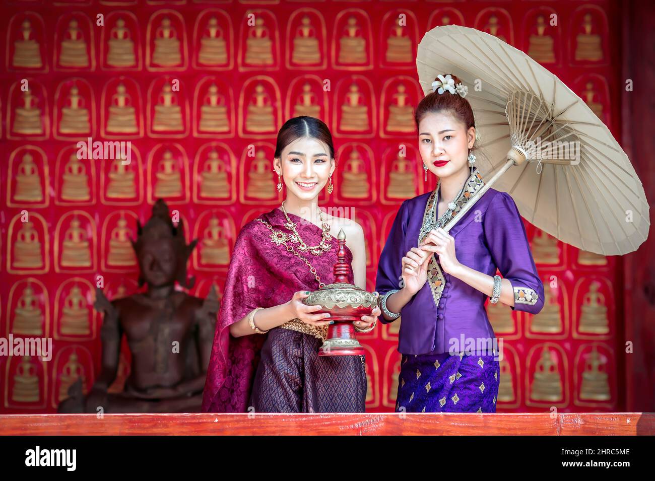 Portrait of two smiling women in traditional clothing standing by a Buddha statue, Chiang Mai, Thailand Stock Photo