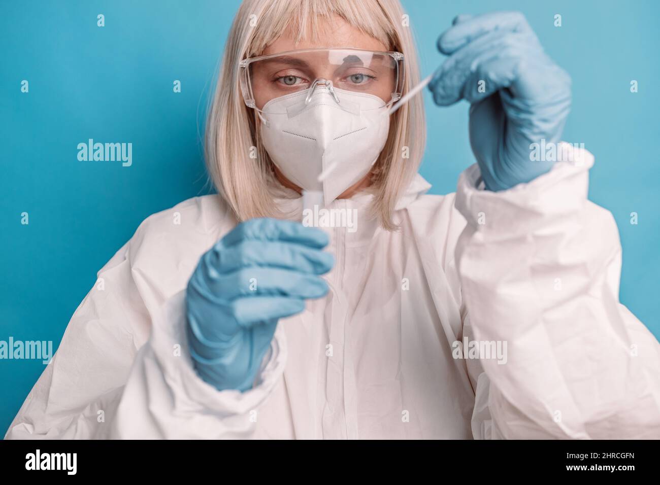 Coronavirus pcr test. Doctor in protective suit medical mask gloves holding Swab saliva sample for diagnostic covid 19 coronavirus virus on blue backg Stock Photo