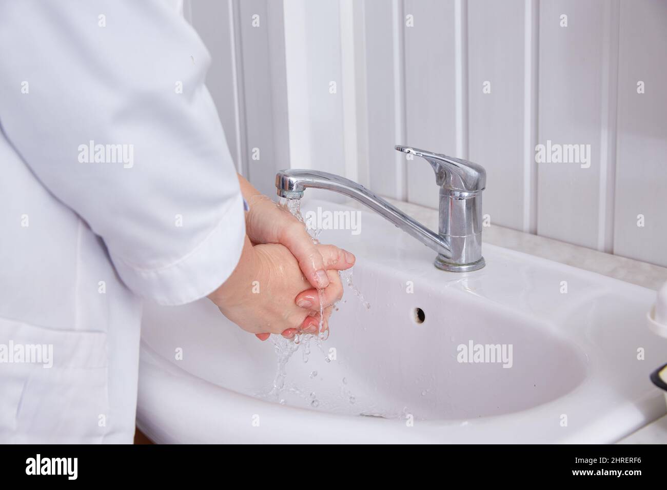 nurse washes her hands in a white sink under running water from the tap. Stock Photo