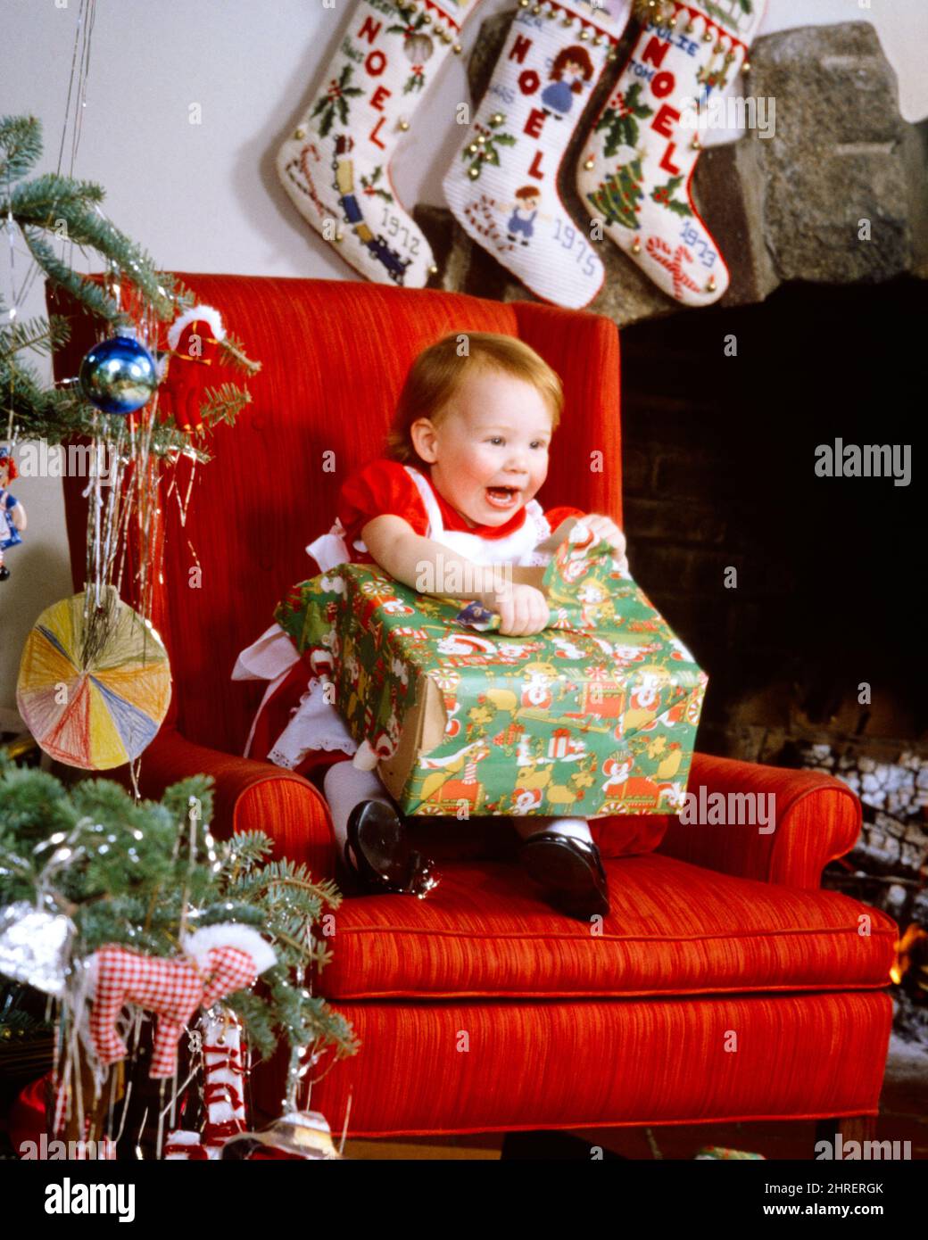 1970s 1980s HAPPY LAUGHING LITTLE GIRL TODDLER SITTING IN BIG RED LIVING ROOM CHAIR BY CHRISTMAS TREE UNWRAPPING A GIFT PRESENT - kx9470 PHT001 HARS LAUGH INFANT DECORATIONS PLEASED JOY LIFESTYLE SATISFACTION CELEBRATION FEMALES HOME LIFE COPY SPACE HALF-LENGTH HAPPINESS CHEERFUL DISCOVERY LIVING ROOM MERRY EXCITEMENT BY IN HOLIDAYS SMILES DECEMBER DECEMBER 25 JOYFUL UNWRAPPING JOYOUS JUVENILES BABY GIRL CAUCASIAN ETHNICITY OLD FASHIONED Stock Photo