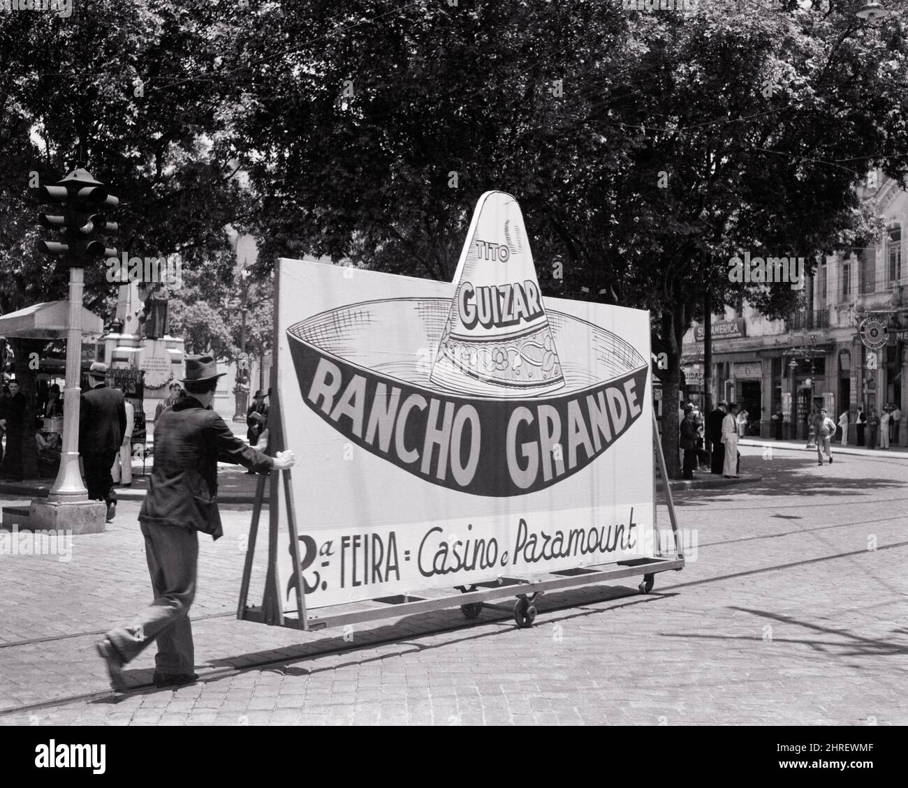 1930s 1940s MAN PUSHING BILLBOARD AD ON WHEELS FOR 1936 MOVIE RANCHO GRANDE TITO GUIZAR PLAYING PARAMOUNT CASINO SANTOS BRAZIL - r12377 PAL001 HARS MALES WHEELS ENTERTAINMENT MEXICAN B&W SOUTH AMERICA PERFORMING ARTS SKILL TEMPTATION OCCUPATION SKILLS ADVERTISEMENT LEISURE AD SOMBRERO RECREATION LABOR ON EMPLOYMENT OCCUPATIONS CONCEPTUAL GRANDE 1936 BRAZIL CASINO STYLISH INFRASTRUCTURE EMPLOYEE RELAXATION YOUNG ADULT MAN BLACK AND WHITE LABORING OLD FASHIONED Stock Photo