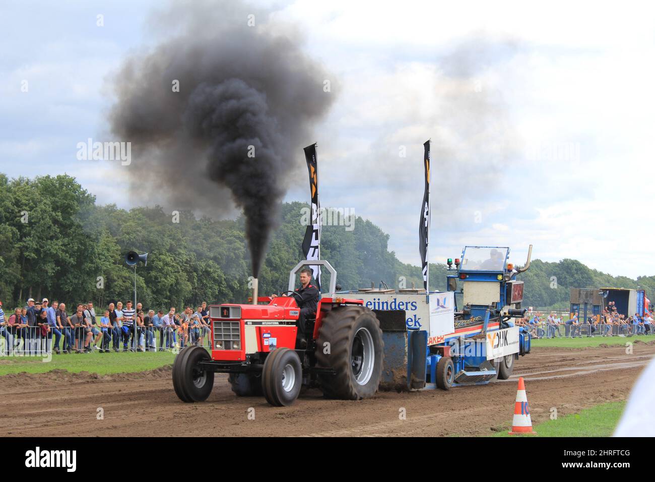 a tractor with a big plume of smoke is driving at the field during tractor pulling at an outdoor event in summer in Holland Stock Photo