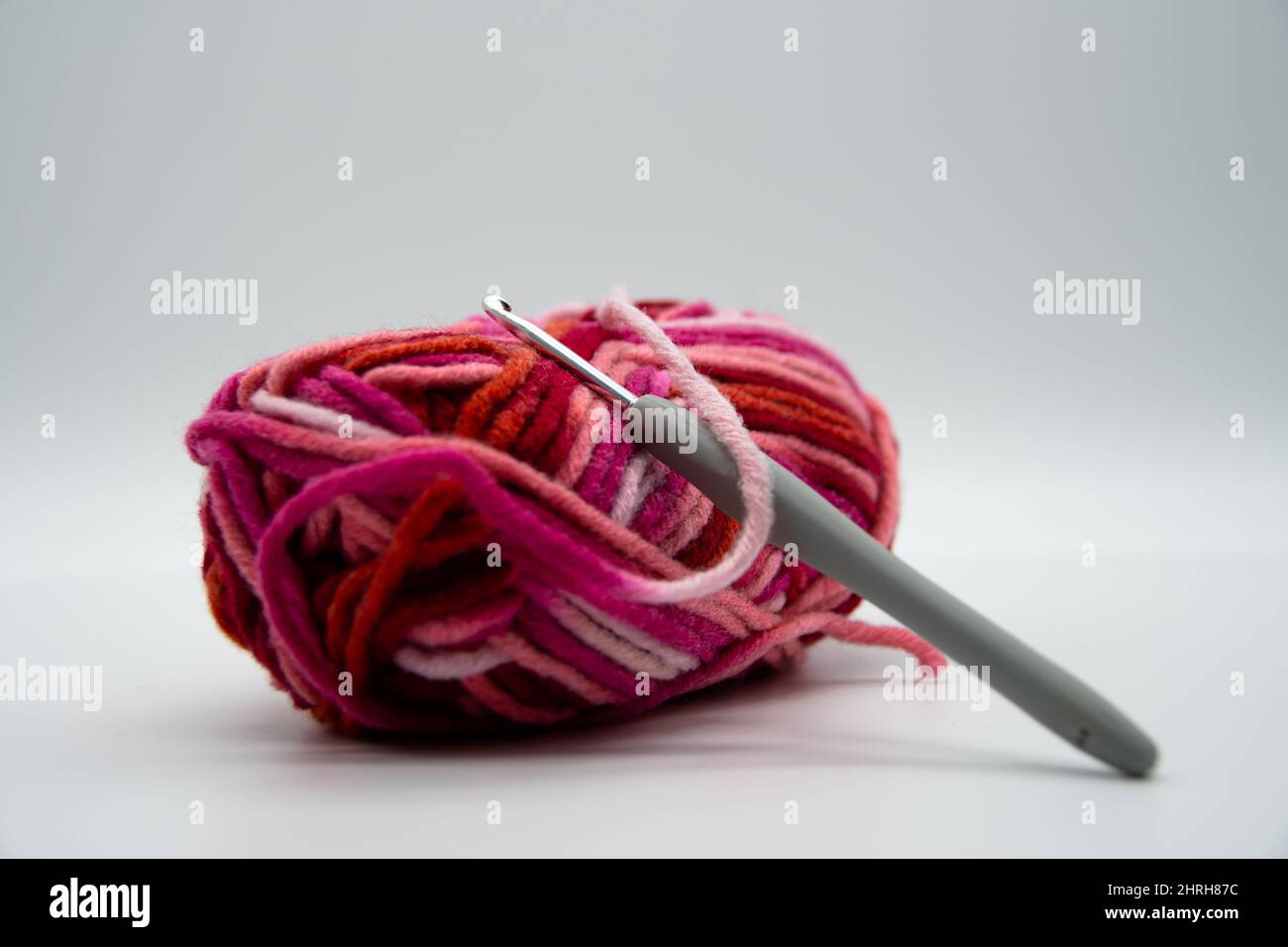 A brightly colored ball of wool with warm colors and a crochet hook Stock Photo