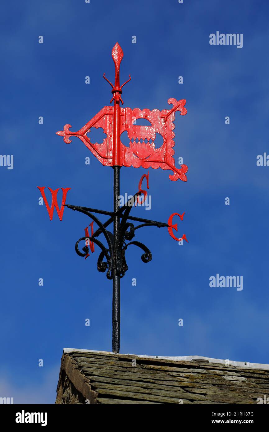 A wind vane, weather vane, or weathercock (black pole with Red flag shaped  body and compass point letters) mounted on a slated roof against a blue sky  Stock Photo - Alamy