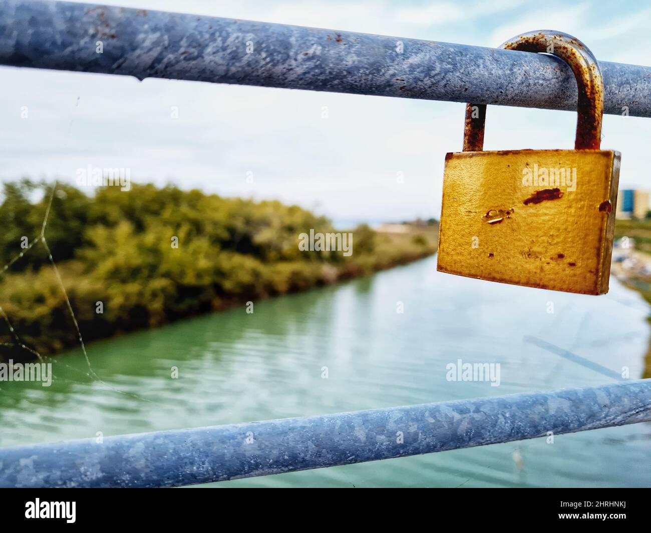 Golden padlock hooked on the railing of the bridge over the river Stock