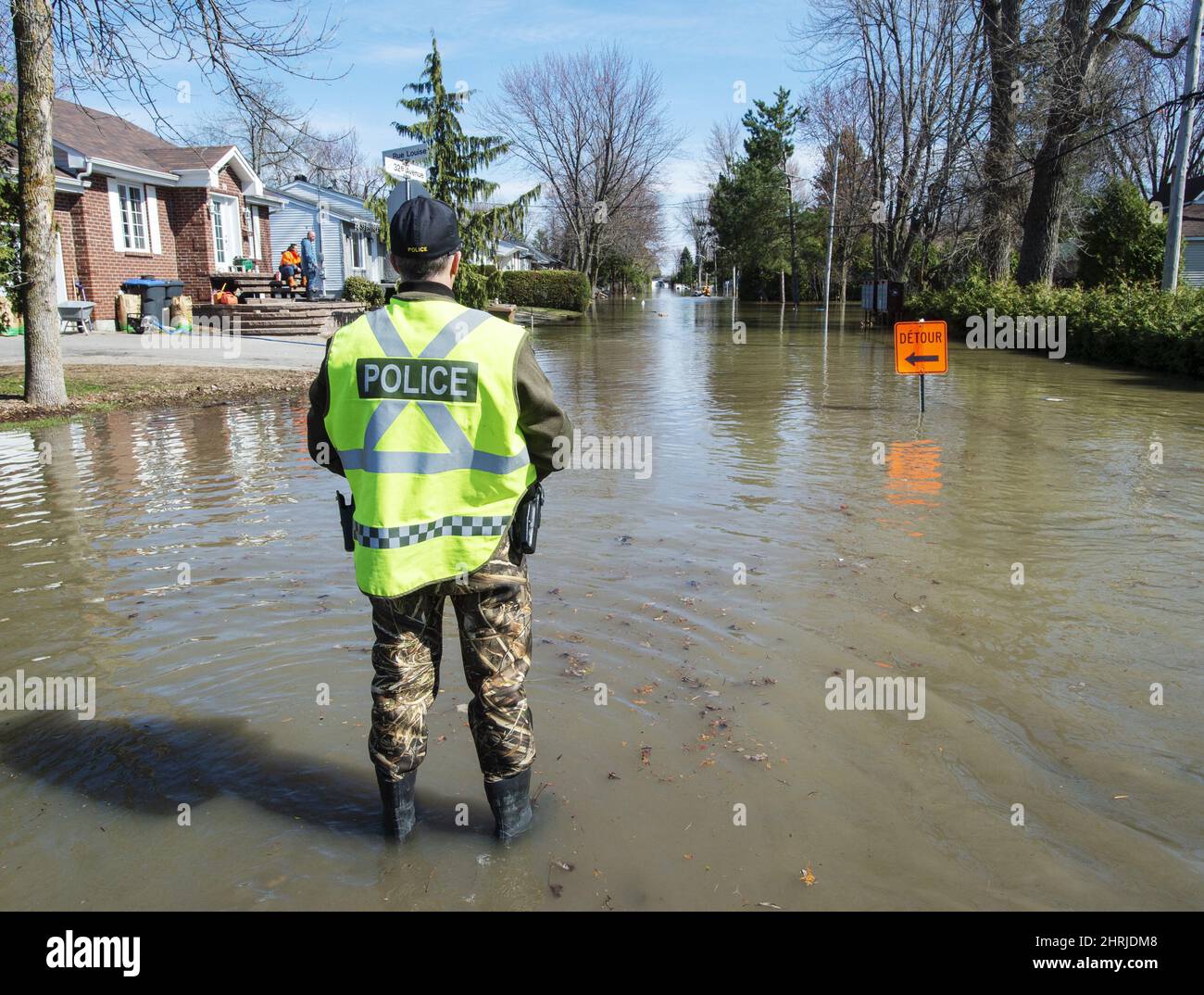 A police officer stands watch on a flooded street after a dike broke ...
