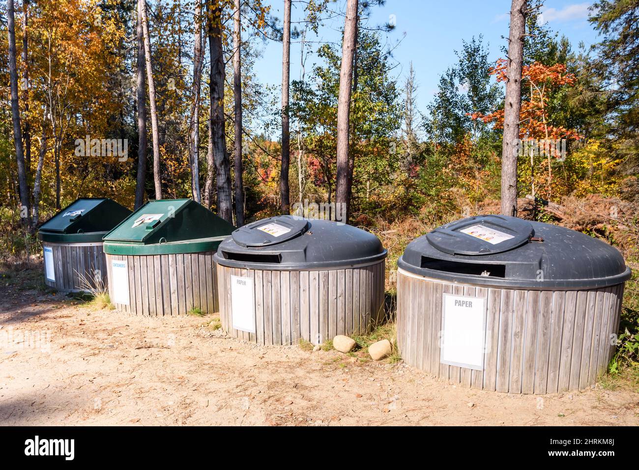 Row of large recycling bins in a recycling centre in the countryside on a sunny autumn day. Autumn colours in background. Stock Photo