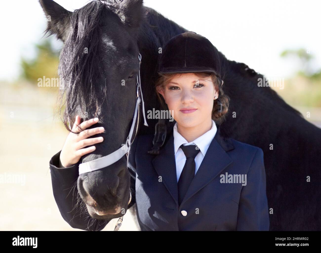 Horse and rider share a strong bond.... Portrait of a young female rider stroking her horses face and smiling proudly at the camera. Stock Photo