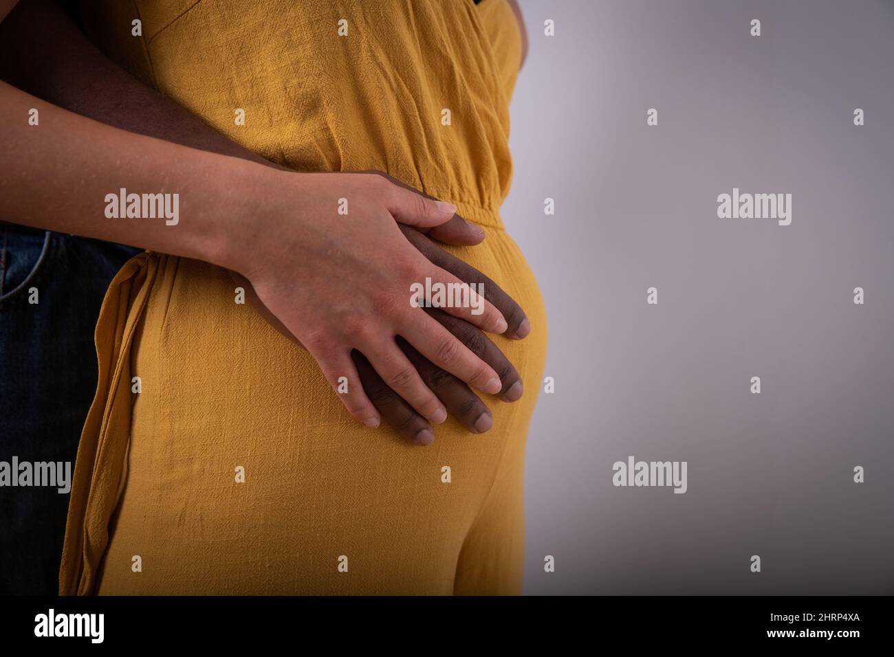 Close-up of the hands of a black man who touches the belly of a white woman, interracial couple is pregnant and expecting a child Stock Photo