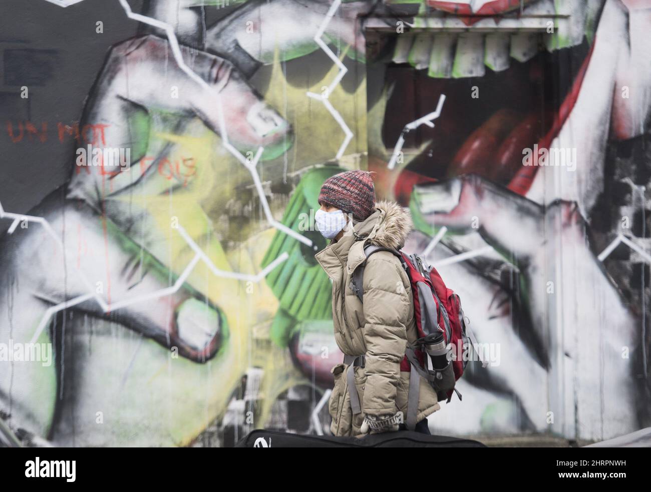 A person wears a face mask as they walk by a mural in Montreal, Sunday