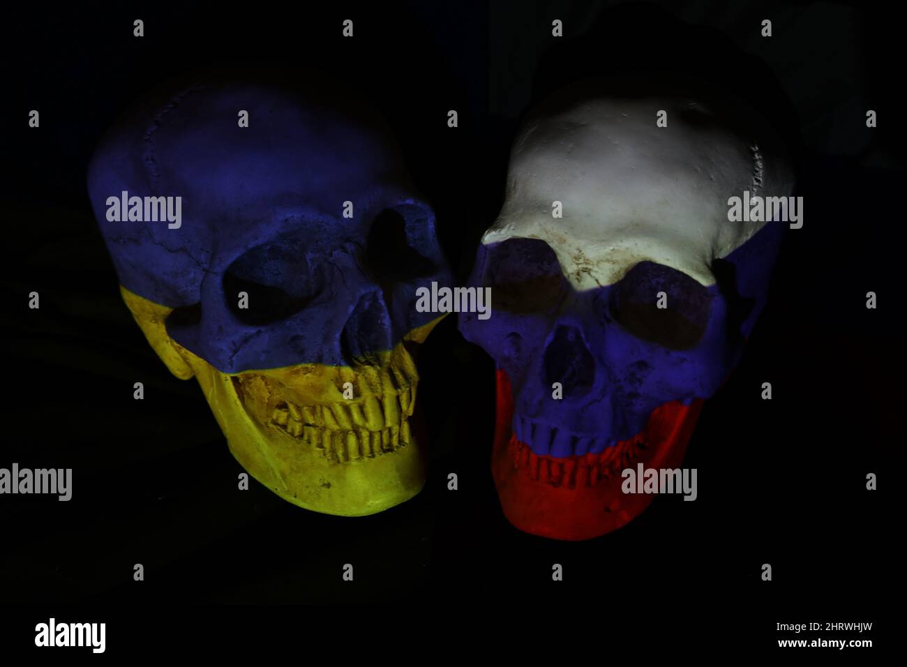 Two opposing skulls colored with the national flags of Russia and Ukraine projected on them. Darkened threatening theme. Conflict war tension concept. Stock Photo