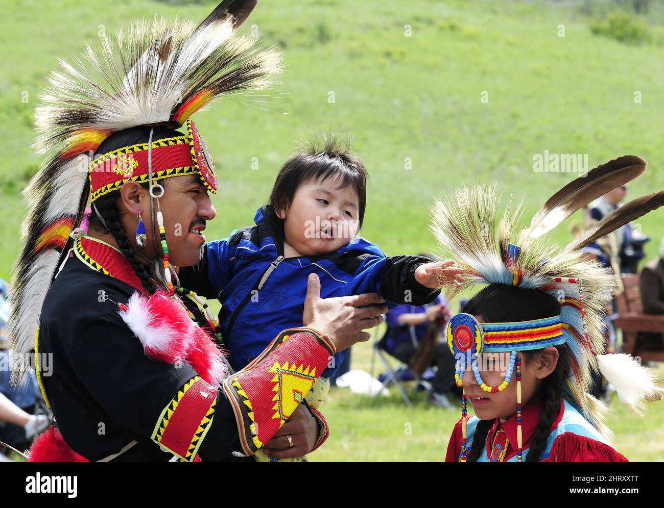 Rider Armstrong, center, 1, reaches for the headdress of Richard Guardipee, 11, from Browning, Mont., as he is held by father Patrick Armstrong, left, also from Browning, Montana, prior to the start of Chicken Dance competitions at Blackfoot Crossing east of Calgary, Canada. on Saturday, June 19, 2010. (AP Photo/The Canadian Press, Larry MacDougal) Stock Photo