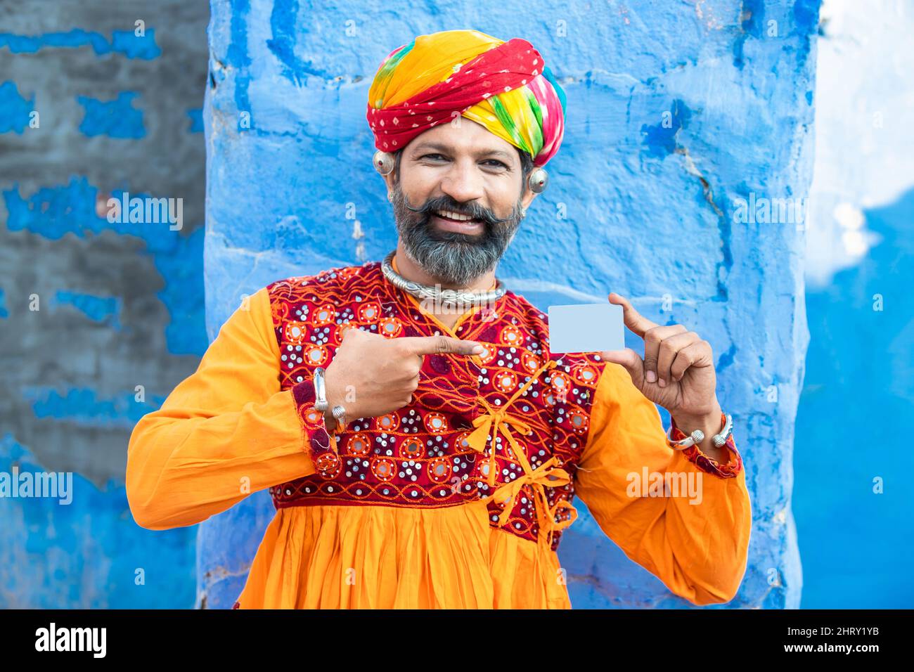 Happy traditional Indian man wearing colorful turban and outfits showing debit credit bank card for advertisement or branding. Beard Male holding empt Stock Photo