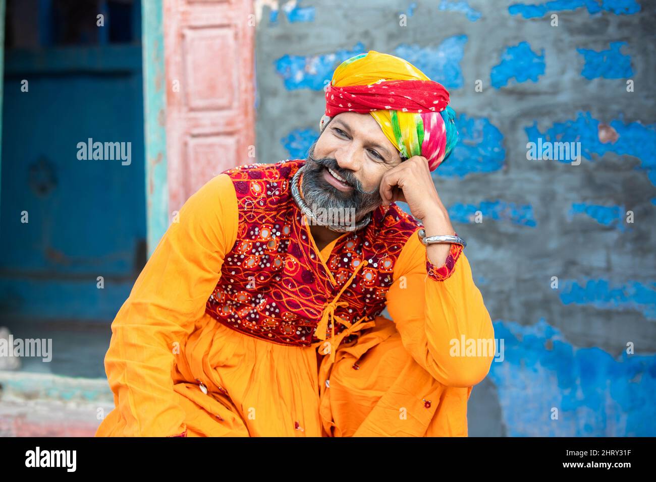 Portrait of happy traditional north indian man wearing colorful attire sitting. Smiling Rajasthan male with turban and ethnic outfits. Culture and fas Stock Photo
