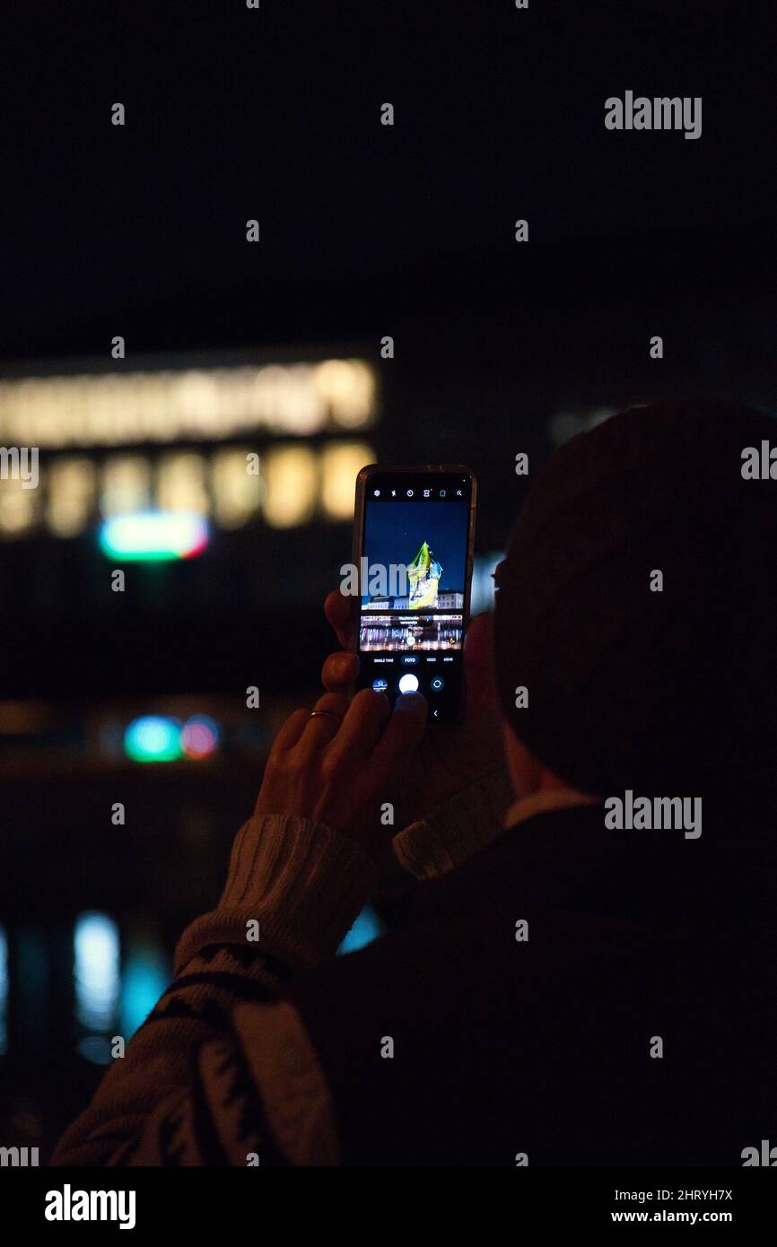 Male shooting by a phone with colorful lights during the Lilu Light Festival in Lucerne at night Stock Photo