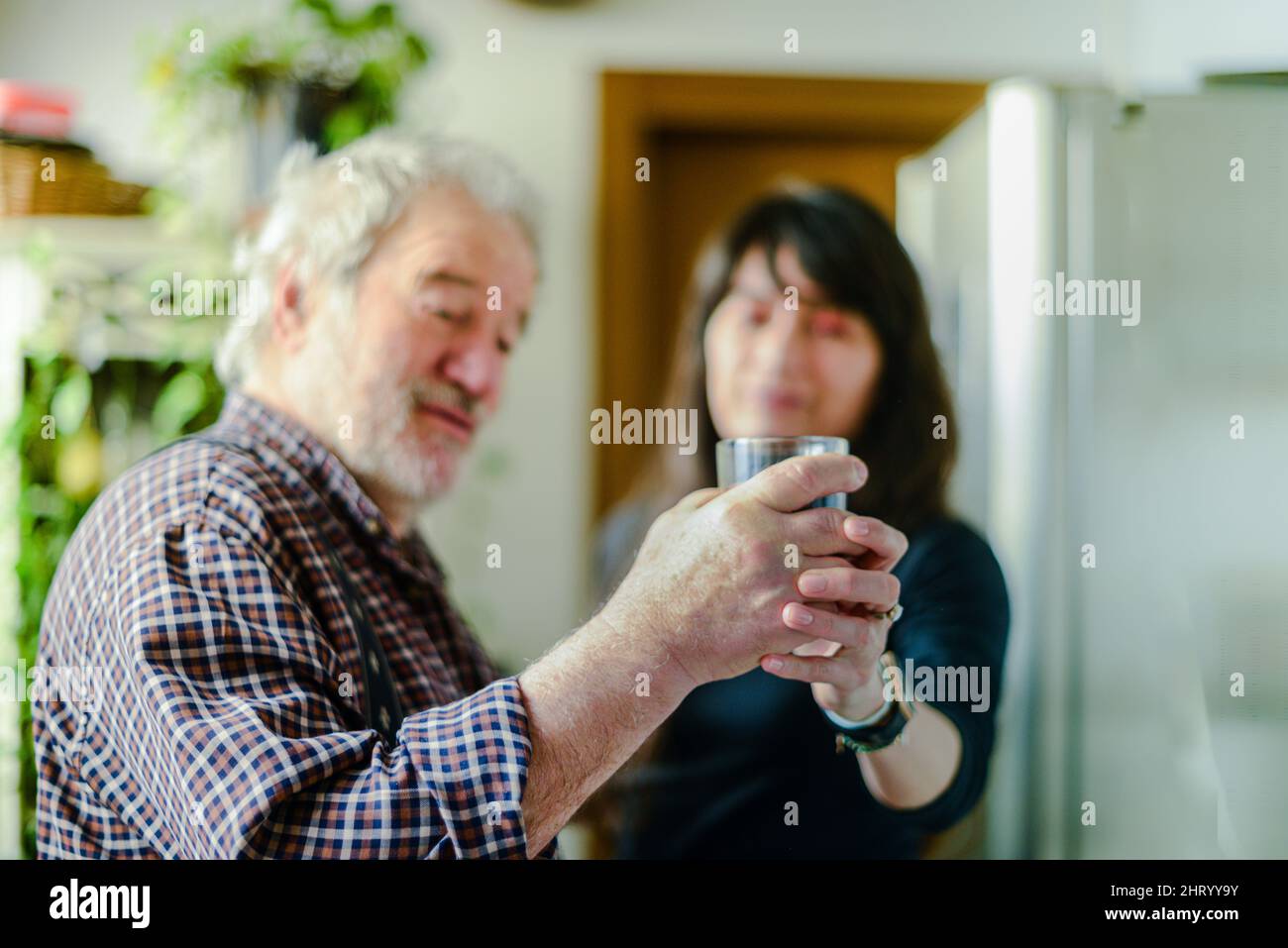 caucasian senior man drinking wine and getting drunk at home stressing younger hispanic wife - alcoholism and domestic violence concept Stock Photo