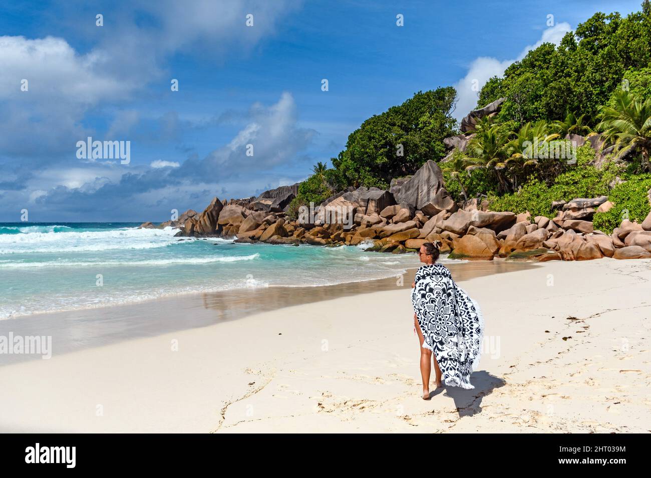 Woman wrapped in towel, standing alone on sandy beach on tropical island of La Digue on