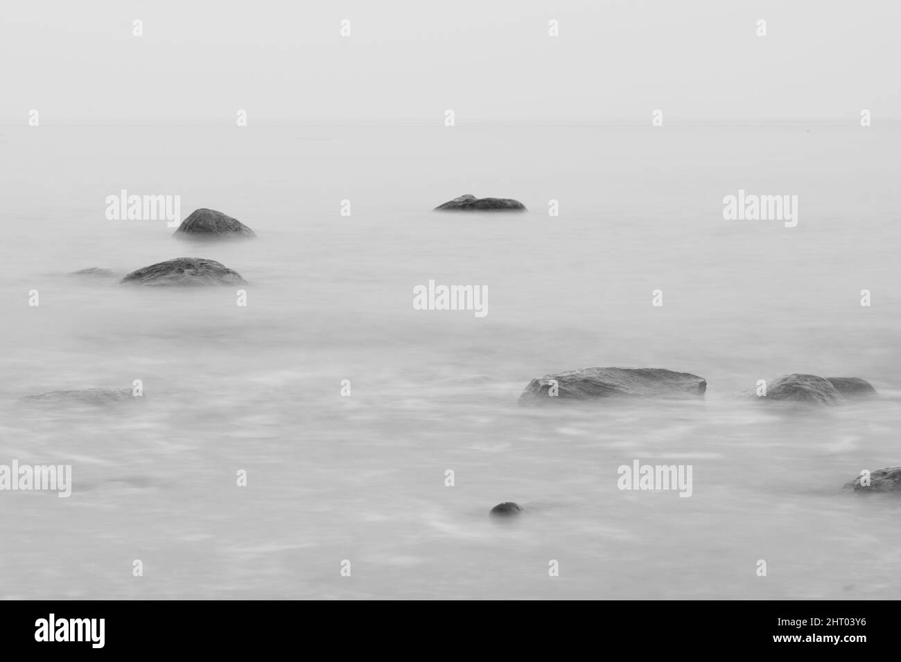 Tranquil scenery of rocks in the sea on a foggy day, grayscale shot ...