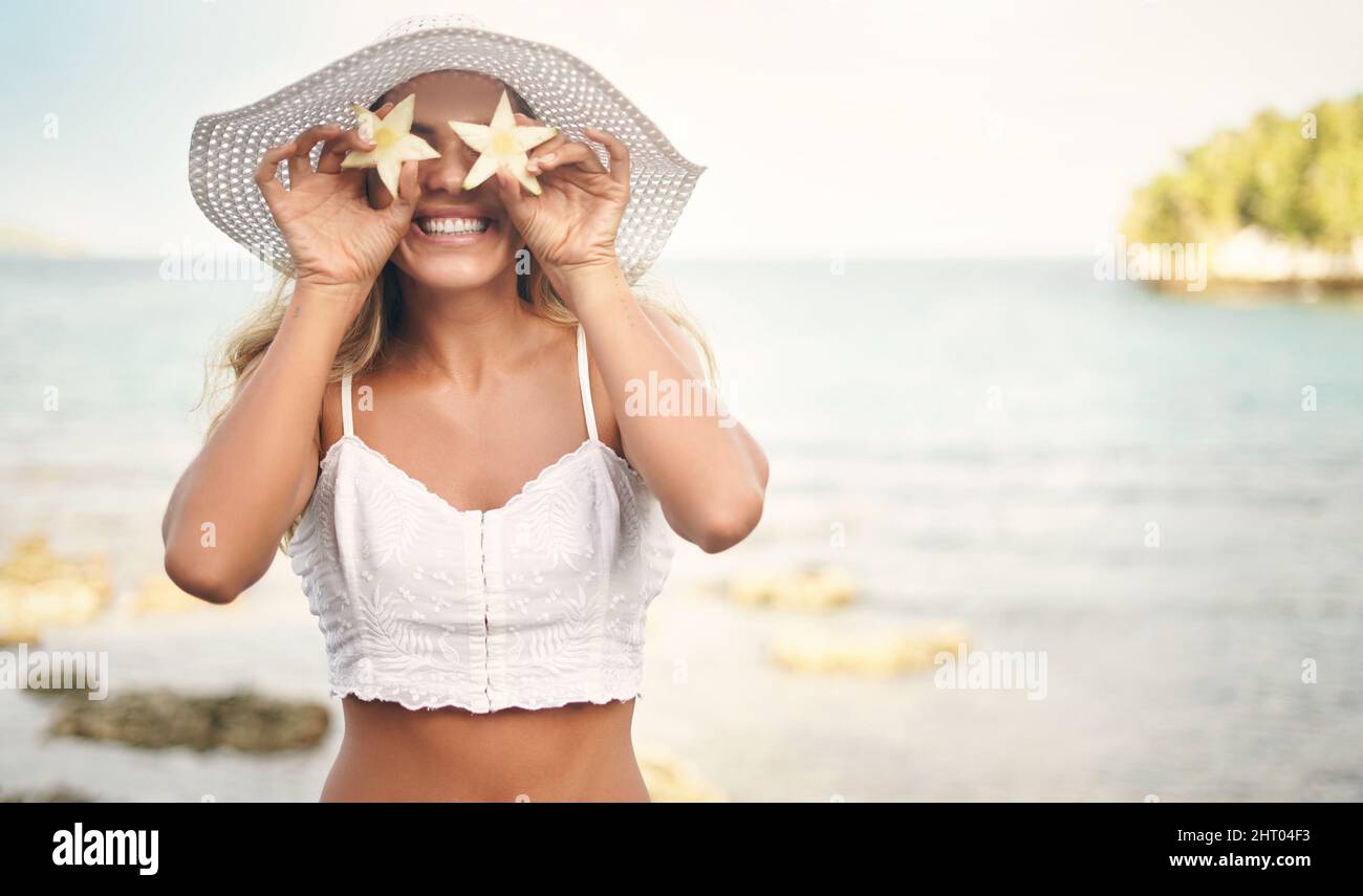 Feeling like a star today. Cropped shot of an attractive young woman standing and playfully holding up star shaped pineapple pieces against her eyes. Stock Photo