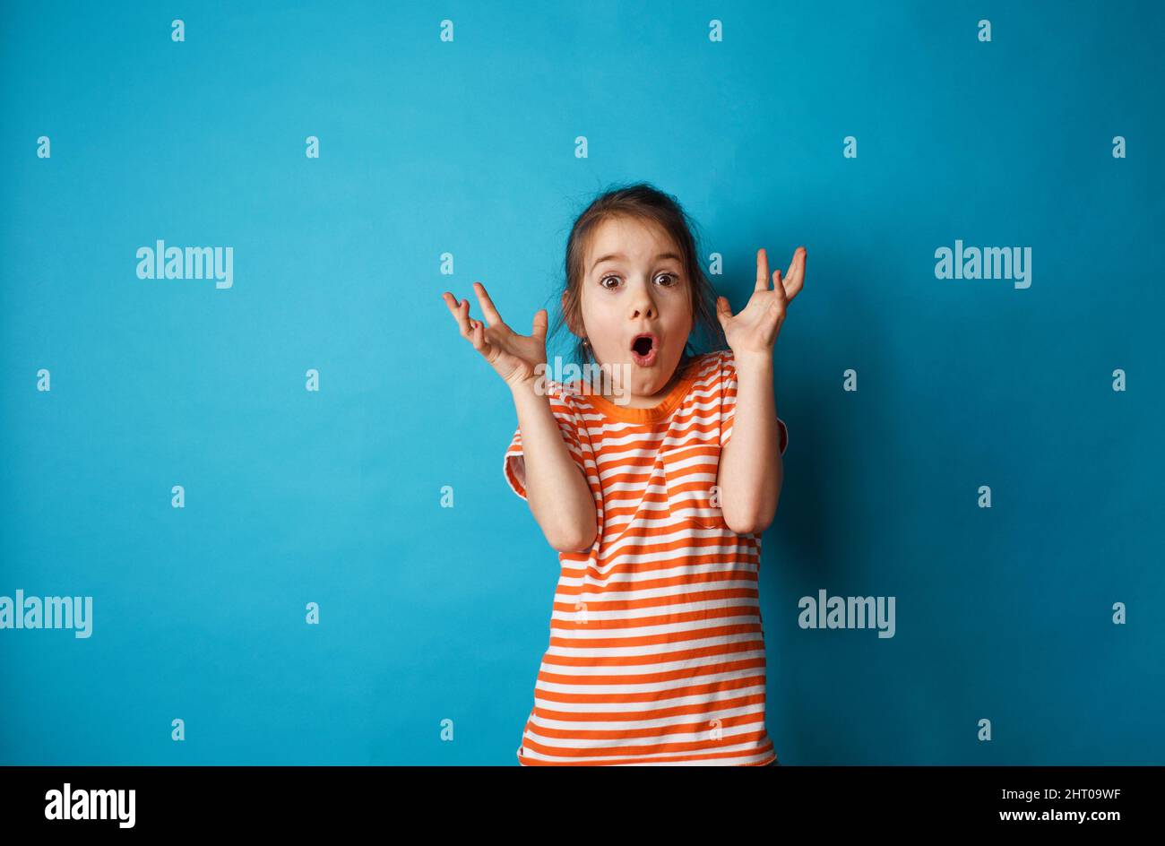 Portrait of a surprised cute little girl standing isolated on a blue ...