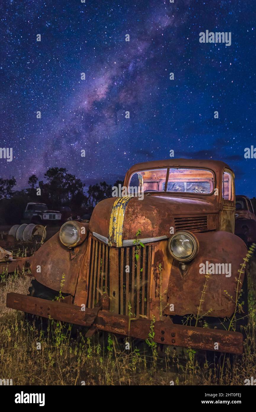An old, vintage ford pick-up lying in a tree-lined grassy paddock with the milky-way core in the background near Chillagoe, Queensland in Australia. Stock Photo