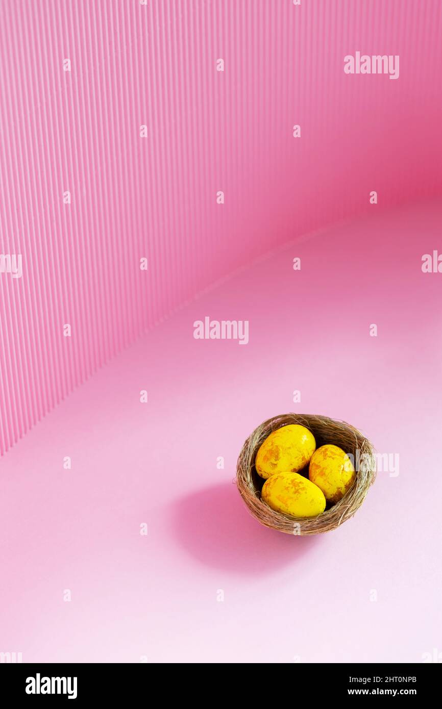 Easter eggs in a natural nest. Painted yellow-golden eggs on a pink background. Easter minimalistic concept. Copy space Stock Photo