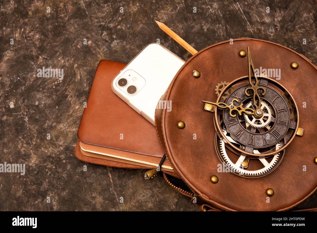 Leather bound sketchbook, pencil and smartphone in a circle clockwork steampunk leather bag on a grungy background. Stock Photo