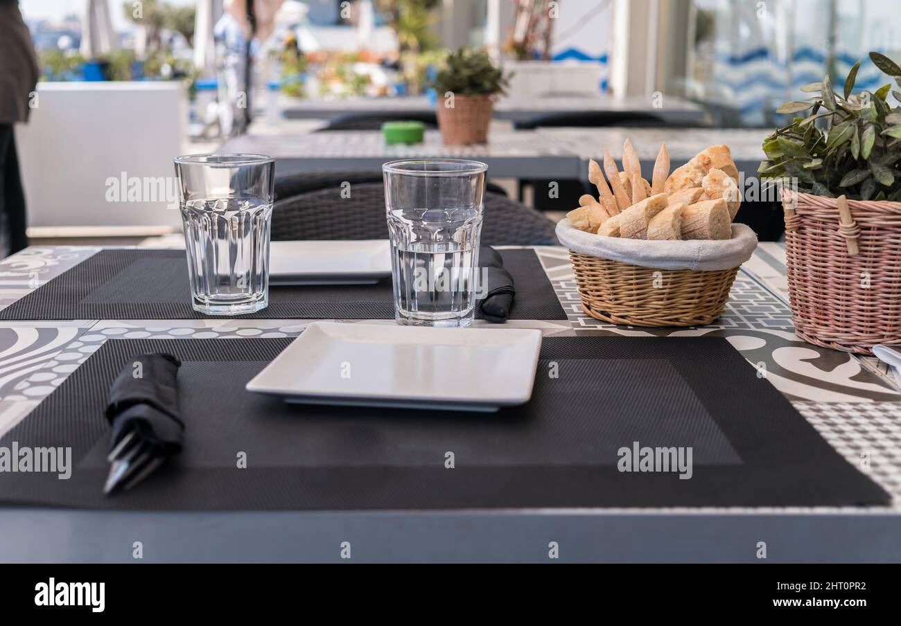 Table prepared on the outside terrace Spanish restaurant, a basket with bread, glasses, plates, and garnished with a plant, Table restaurant terrace Stock Photo