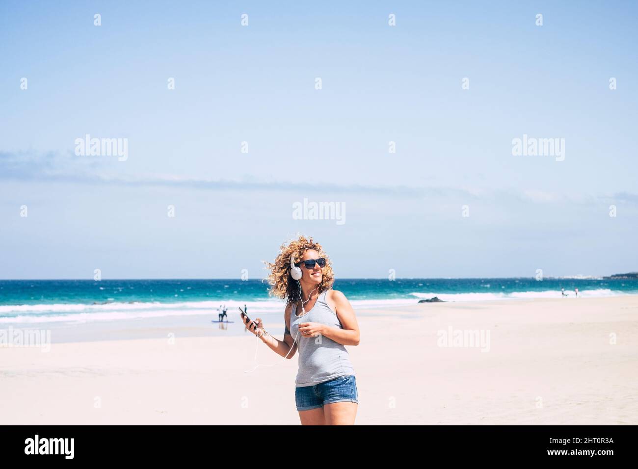 Happy female tourist enjoy leisure outdoors at the beach listening music from mobile phone and headset amiling and enjoying summer holiday vacation tr Stock Photo
