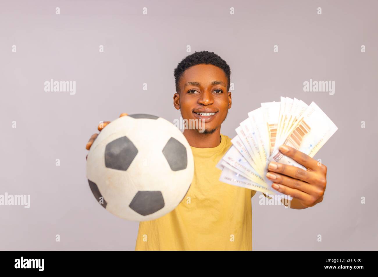 Sport bet excitement, gambing and family lifestyle concept. Excited african-american young guy enjoying their win, standing with soccer ball and lots Stock Photo