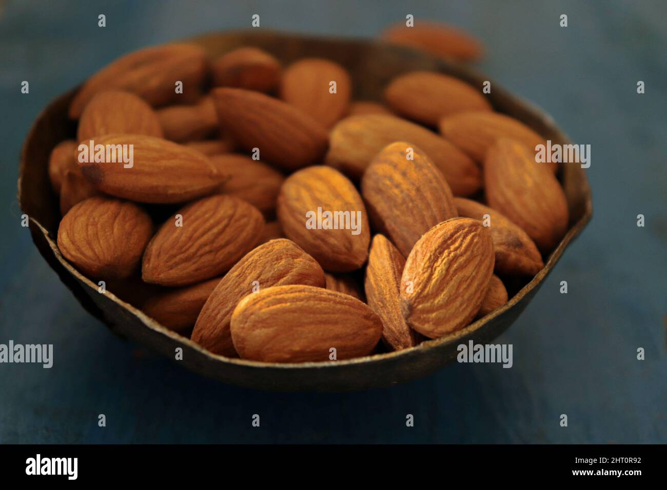 Close-up of  almonds in a copper bowl against blue background Stock Photo
