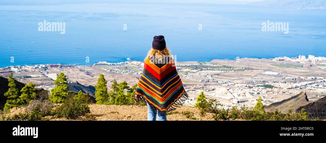 Woman admiring beautiful panorama landscape and wearing colorful trendy poncho. Tourist and traveler people viewed from back enjoying freedom and amaz Stock Photo