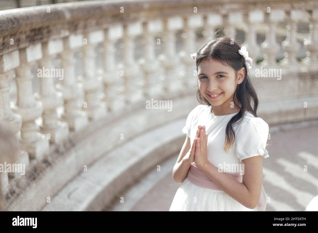 portrait of girl in communion dress with hands in prayer pose looking at camera with copy space Stock Photo