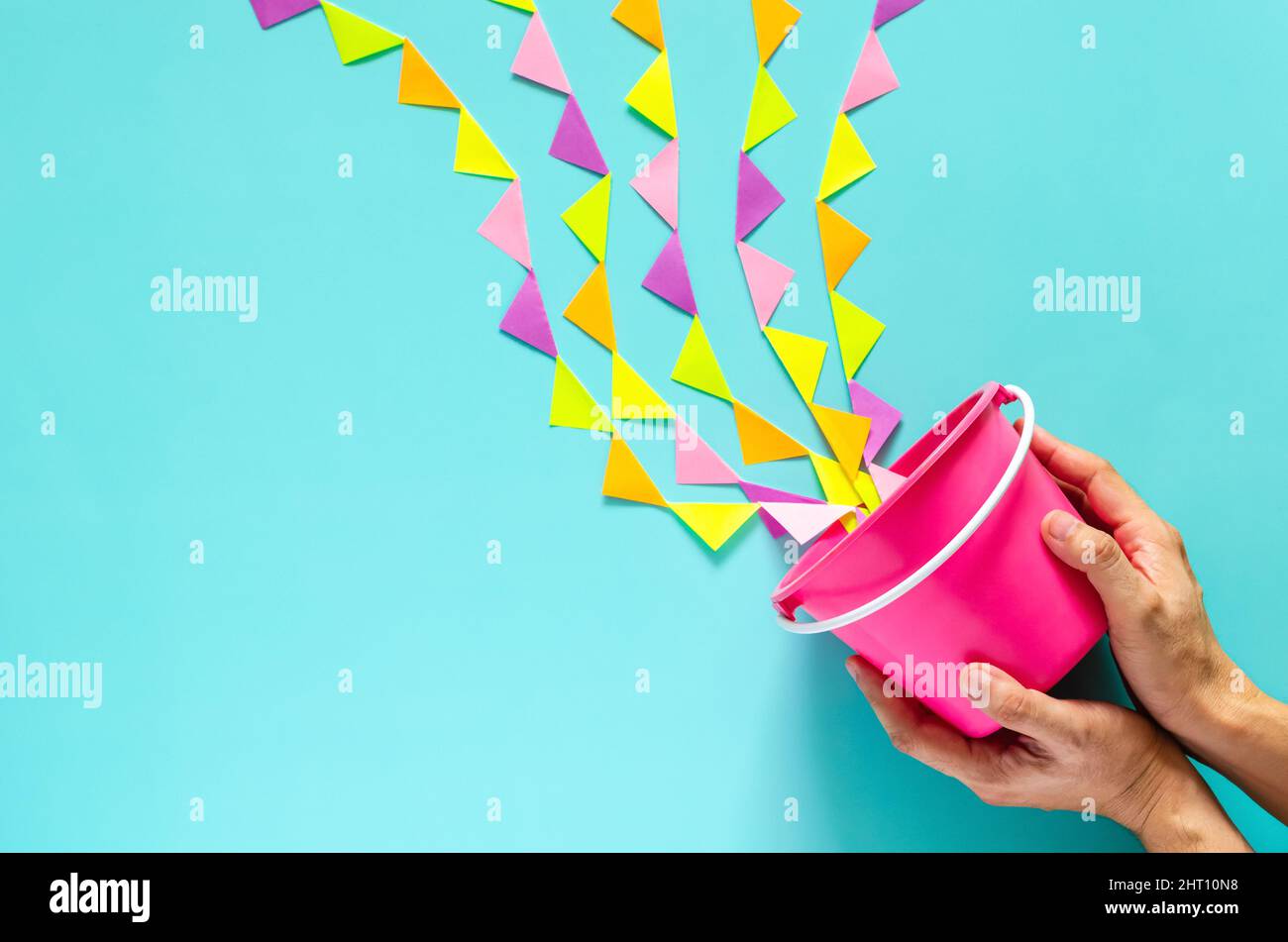 Hand holding pink bucket splash out with colorful party flag that set as water for Songkran festival celebration on blue background. Minimal holiday c Stock Photo