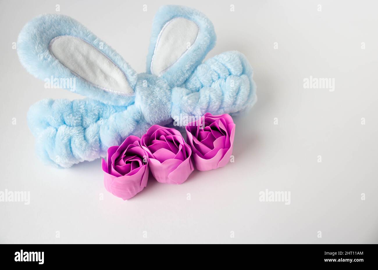 A blue headband with rabbit ears and pink soap roses. Body care. Easter concept. Place for your text. Stock Photo
