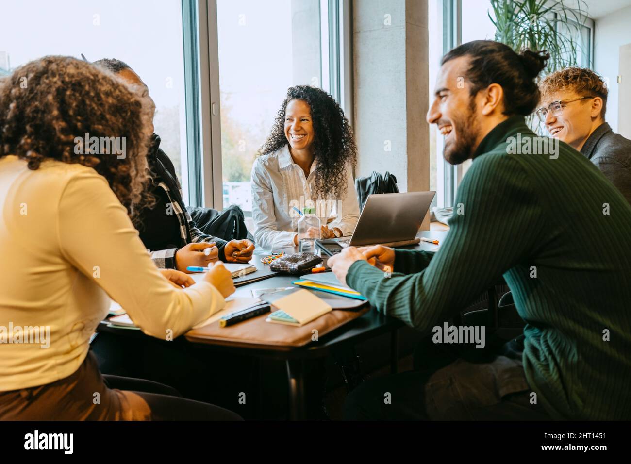 Cheerful students talking while sitting at table in cafeteria Stock Photo
