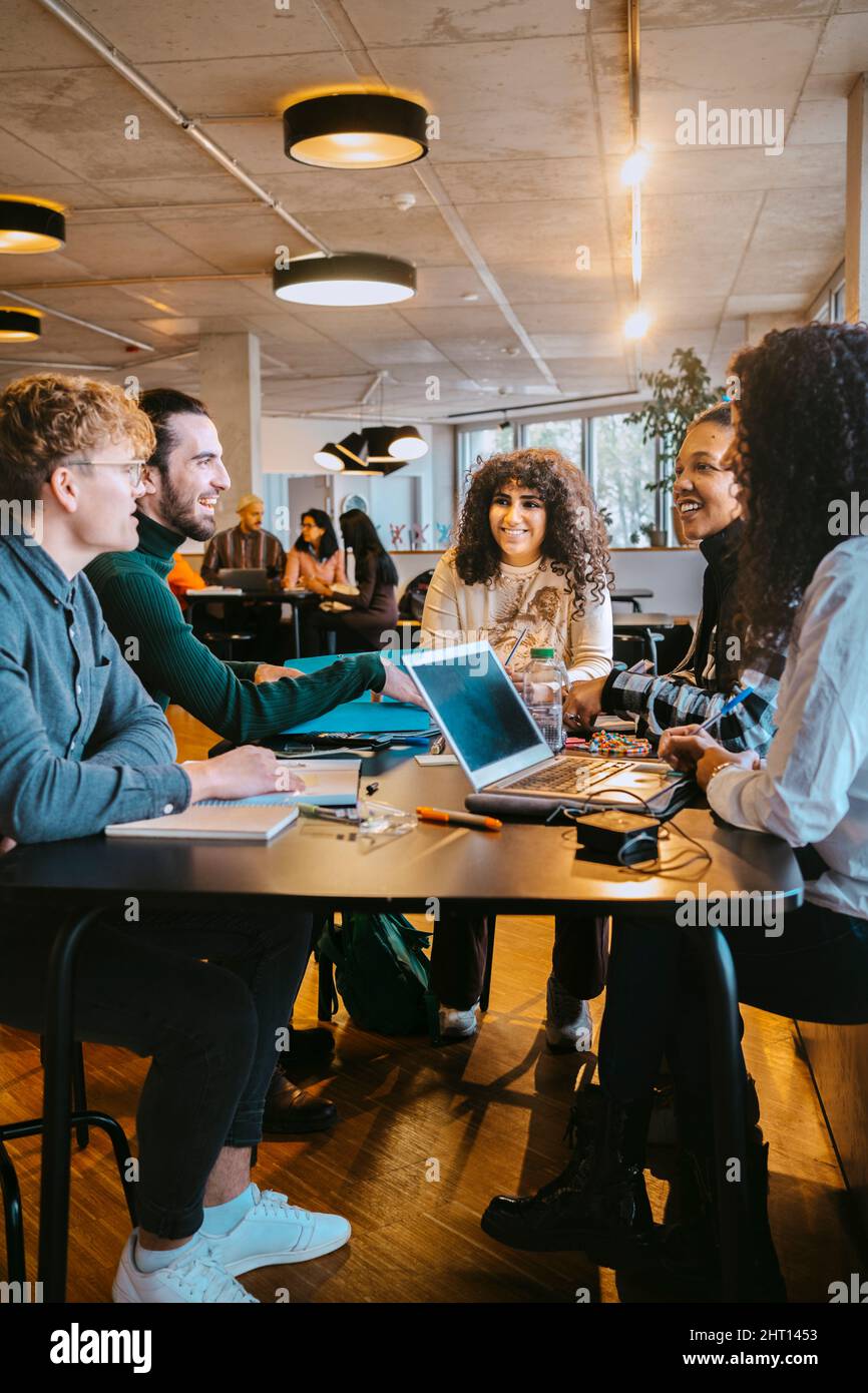 Smiling students talking while sitting at table in cafeteria Stock Photo