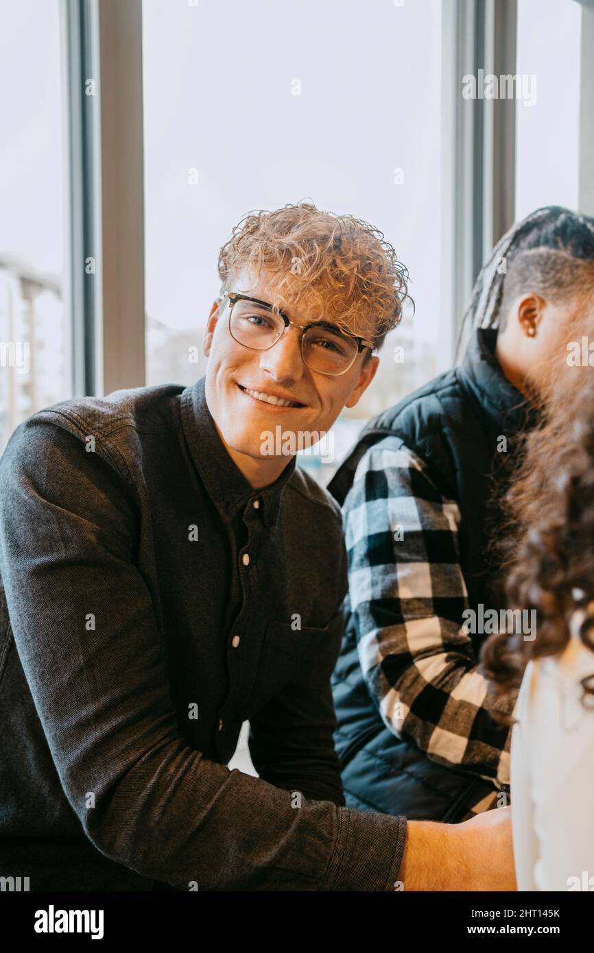 Portrait of smiling blond man wearing eyeglasses sitting at cafeteria in university Stock Photo