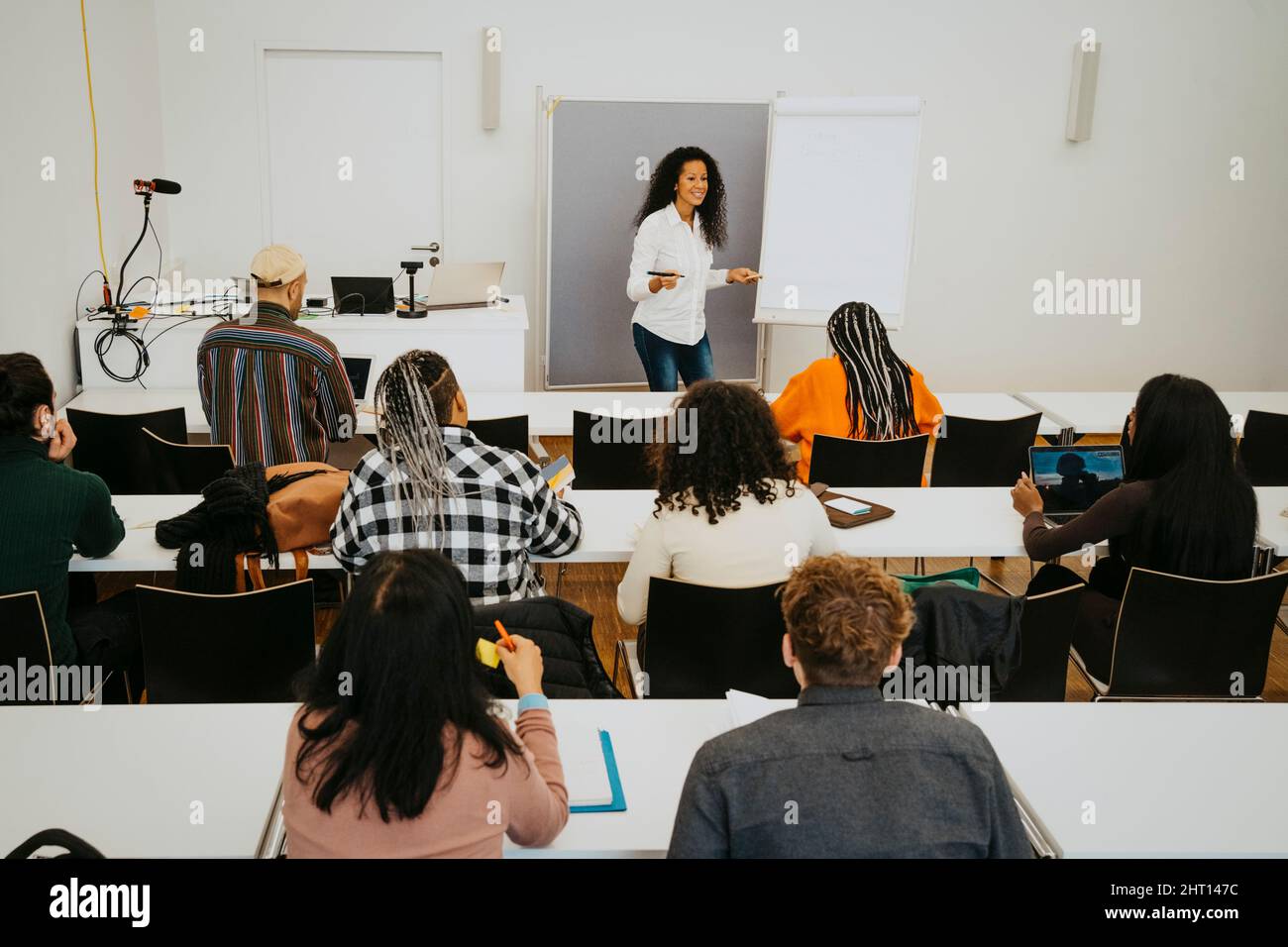 Smiling professor teaching students while standing by flipchart in classroom Stock Photo