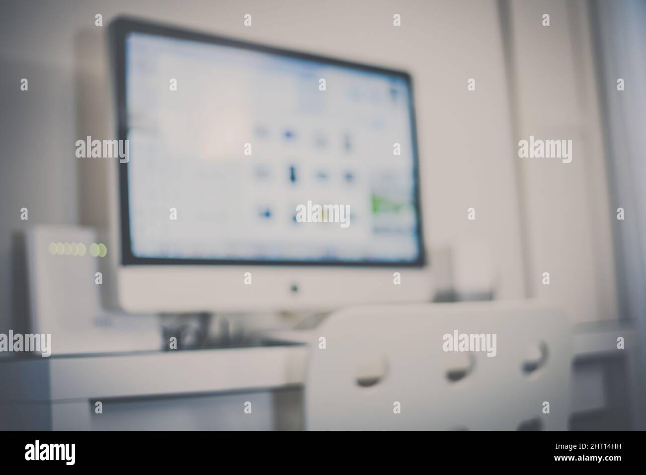 Blurred view of a desk with computer in a modern home interior. Out of focus big monitor on the table ready to work or study in a remote station. Home Stock Photo